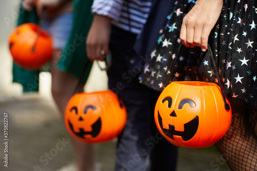 Close-up of children with pumpkins bags playing trick or treat outdoors