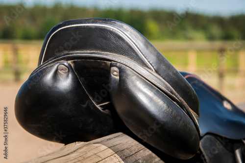 Black leather saddle on a wooden fence.