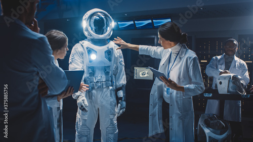 Diverse Team of Aerospace Scientists and Engineers Wearing White Coats have Discussion, Use Computers Design New Space Suit Adapted for Galaxy Exploration and Travel. Constructing Astronaut Suit
