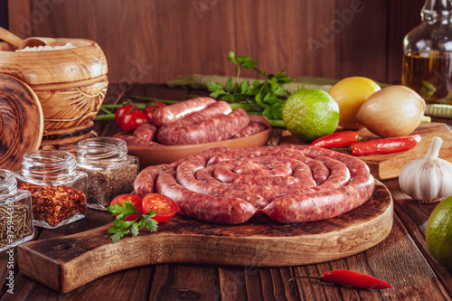Raw thin brazilian sausages on the wooden board with ingredients - Linguiça toscaninha