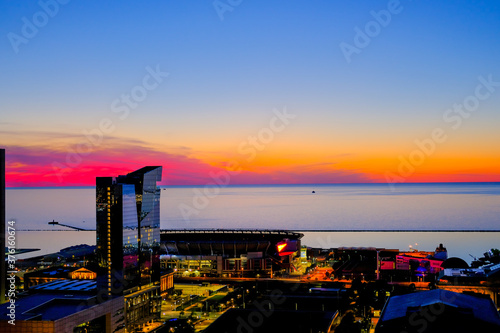 Sunset view over Lake Erie with Cleveland cityscape covered in pink, purple and orange shades with illuminated streets and buildings