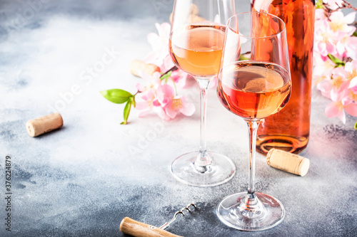 Rose wine glass with bottle on the gray table and pink flowers. Rosado, rosato or blush wine tasting in wineshop, bar concept. Copy Space