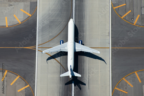 Aerial view of narrow body aircraft departing airport runway. Top down view of white unidentified airplane in the center of taxiway lines. Aviation industry.