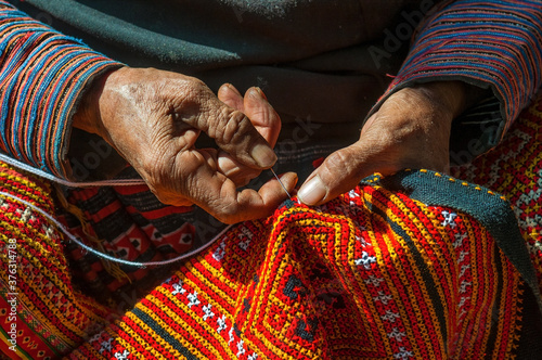 Hands of a Black Hmong woman sewing colorful traditional fabric and other arts and crafts with her hands in the sunlight, North Vietnam.