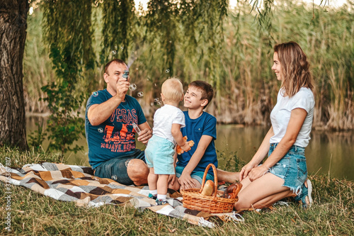Happy family with two children blow soap bubbles on a picnic