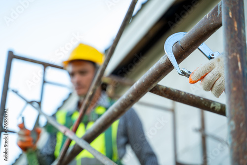 Professional worker wearing safety harness and safety line working on scaffolding at construction site.