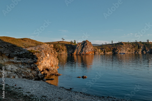 Oranges stones rocks in the light of the setting sun, by the bay with the shore, coast on blue lake Baikal, reflection