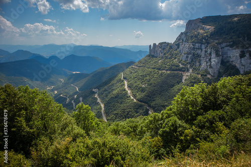 View from Col de Rousset in France. Winding road with twisties and sharp turns viewed from observation point on a cloudy day with some trees in the background.