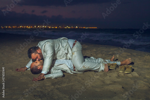 Gay couple kiss on the beach lying on the sand at night