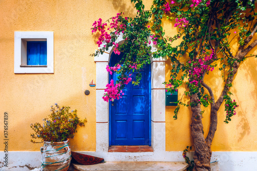 Traditional street with greek houses with flowers in Assos, Kefalonia island. Traditional colorful greek houses in Assos village. Blooming fuchsia plant flowers. Kefalonia island, Greece
