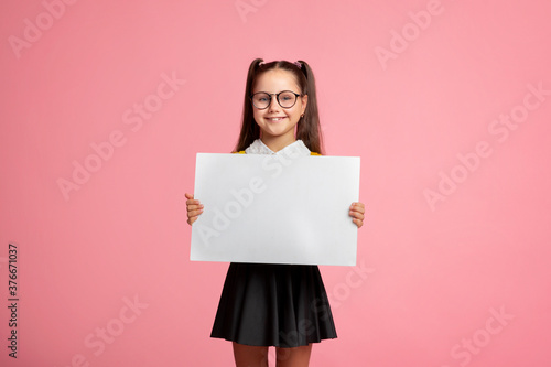 Cheerful child schoolgirl in uniform and glasses holds sign with empty space