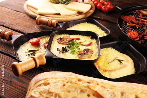 Delicious traditional Swiss melted raclette cheese served in individual skillets with salami and bacon