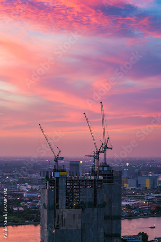 Industrial construction cranes at construction site with sunset sky background