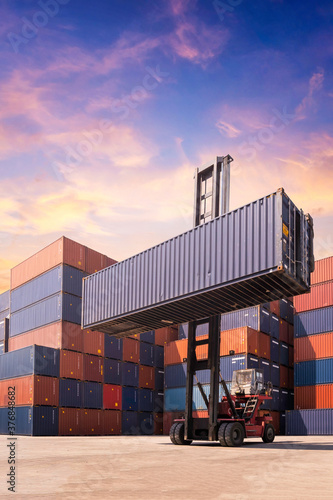 Forklift truck lifting cargo container in shipping yard or dock yard against sunrise sky with cargo container stack in background for transportation import,export and logistic industrial concept