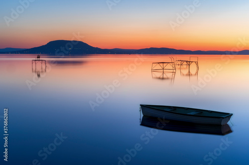 Relaxing and calm sunrise at lake balaton in hungary. Boat and fisher posts. Mountain Badacsonyi and city Badacsony