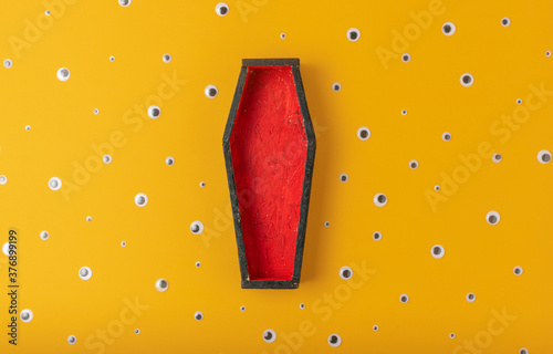 Halloween yellow background with an open red-black coffin in the center, around a scattering of plastic eyes of different sizes. A place for your product.