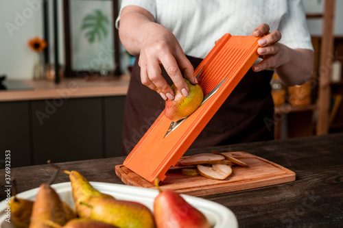 Close-up of unrecognizable woman making pear slices using mandolin slicer while cooking at kitchen