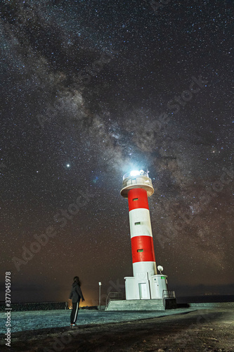 A young woman at the Fuencaliente Lighthouse with the milky way on the route of the volcanoes south of the island of La Palma, Canary Islands, Spain