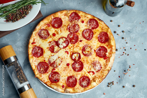 Pizza baked in a wood oven with melted cheese and chorizo salami on a gray background in a composition with cooking ingredients. Top view, food flat lay