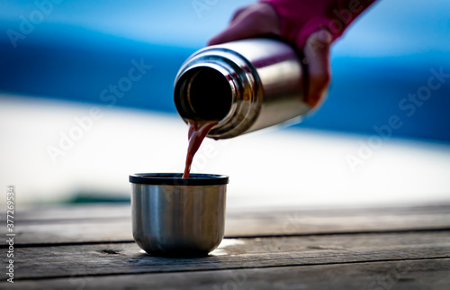 Hiker pouring a hot drink from a metal thermos bottle into a steel mug.