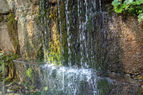 Close up of mountain stream flowing down in summertime. Manmade decorative waterfall flows on rock and splashes
