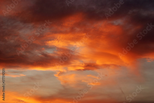 Dark blood red sky background. Dramatic heavy clouds with the hint of the sun at sunset. Many orange tones and patterns of clouds