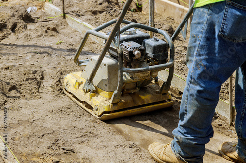 Worker use vibratory plate compactor under construction on new pavement