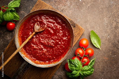 Classic homemade Italian tomato sauce with basil for pasta and pizza in the pan on a wooden chopping board on brown background, top view.