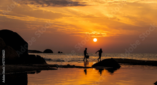 Two person walking across a rocky beach with beautiful sunrise as a backdrop