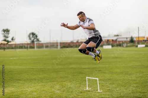 Dedicated strong attractive fit soccer player jumping over obstacle.