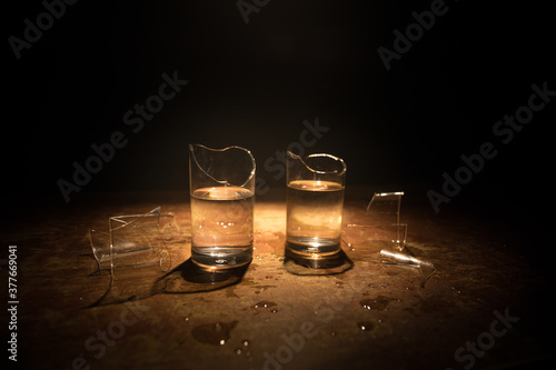 Broken glasses on wooden table at dark toned background with fog. Selective focus