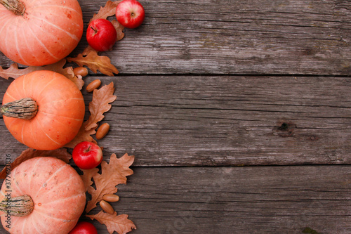 Orange pumpkins, red apples, dry oak leaves, acorns on rough rustic wooden table background. Top view, copy space. Autumn, holiday, thanksgiving, harvest season concept.