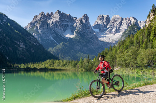 nice and active senior woman riding her electric mountain bike at Duerrenstein Lake in the Hoehlenstein valley between Toblach and Cortina Dampezzo, Three Peaks Dolomites, South Tirol, Italy