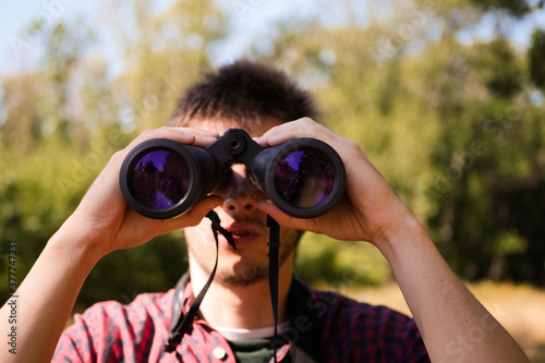 Man in plaid short look through binoculars. Forest hiking. Bird watching. Searching for opportunities concept. Adventure quest 