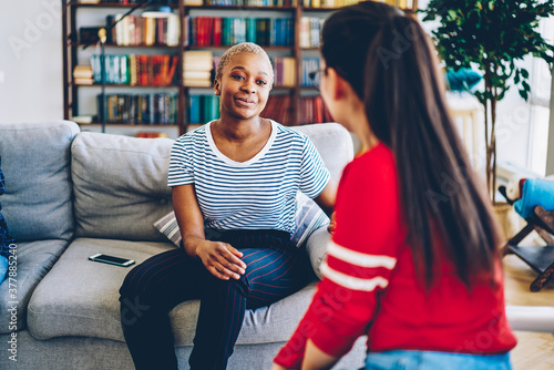 Delighted black woman talking to female friend at home