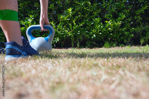 Fitness kettlebell woman cross training outside on crass lifting kettlebells and resistance band for squat