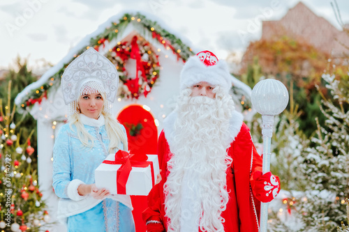 Santa Claus and snow maiden with a gift in their hands pose in the snow