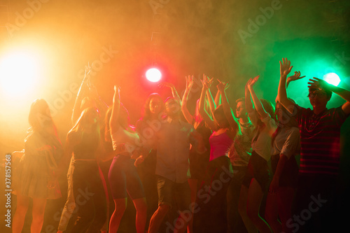 Party time. A crowd of people in silhouette raises their hands, dancing on dancefloor on neon light background. Night life, club, music, dance, motion, youth. Bright colors and moving girls and boys.