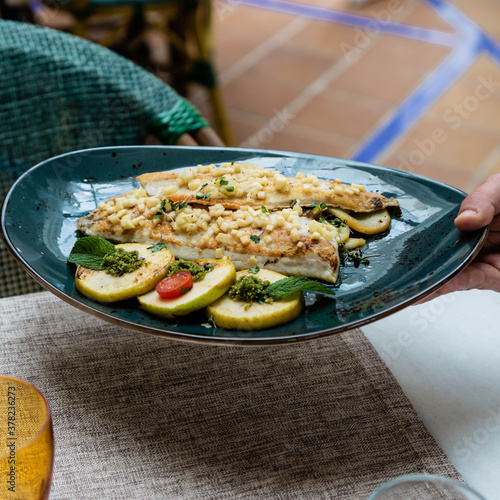 Fish with potatoes on a blue plate on a table.