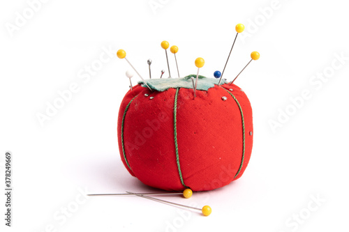 close up of a red pin cushion full of straight pins and yellow quilt pins isolated on white