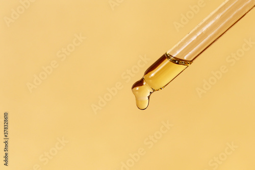 Pipette with falling drop of oil. Dropper with lotion, essence, serum, emulsion. Horizontal monochrome banner, poster, copy space, beige yellow background. Natural organic cosmetic. Body care concept