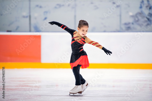 Little girl ice skater in beautiful black red dress ice skating of an indoor ice arena.