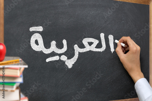 Hand writing on a blackboard in a Arabic language learning class course with the text "Arabic" written on it. with Some books and school materials concept.