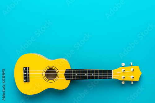 Overhead photo of ukulele with copy space. Yellow colored wooden ukulele guitar on the turquoise blue background.
