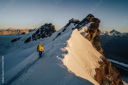 An alpinist climbing a rocky and snow mountain ridge during sunrise. Mountaineering and alpinism in Switzerland. Ascent of Breithorn, Zermatt. Alpine mountain landscape with snow and rocks.