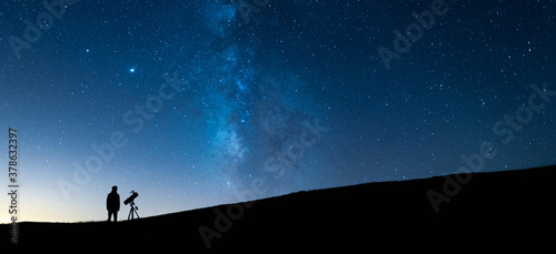 Person observing the blue starry sky with a telescope at night. Silhouette of an astronomer observing the immensity of the universe and the Milky Way