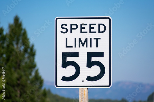 Fifty-five mph speed limit sign. Speed zone traffic sign against blurred tree landscape and blue sky