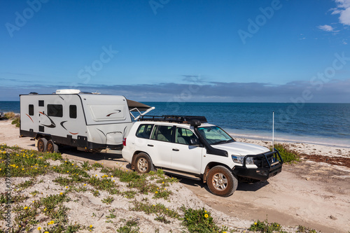 Landscape view of 4WD and modern caravan parked adjacent to a sparkling sunny beach.