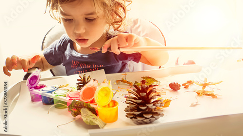 Toddler boy is home schooled painting yellow leaves and pine cones in fall with eco friendly paint. Sensorial activity at home.