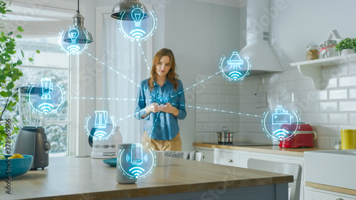 Internet of Things Concept: Young Woman Using Smartphone in Kitchen. She controls her Kitchen Appliances with IOT. Graphics Showing Digitalization Visualization of Connected Home Electronics Devices